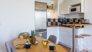 A compact kitchen with a refrigerator, microwave, and a dining area with a table set for breakfast. - Le Flamingo - Première conciergerie (Palavas-les-Flots)