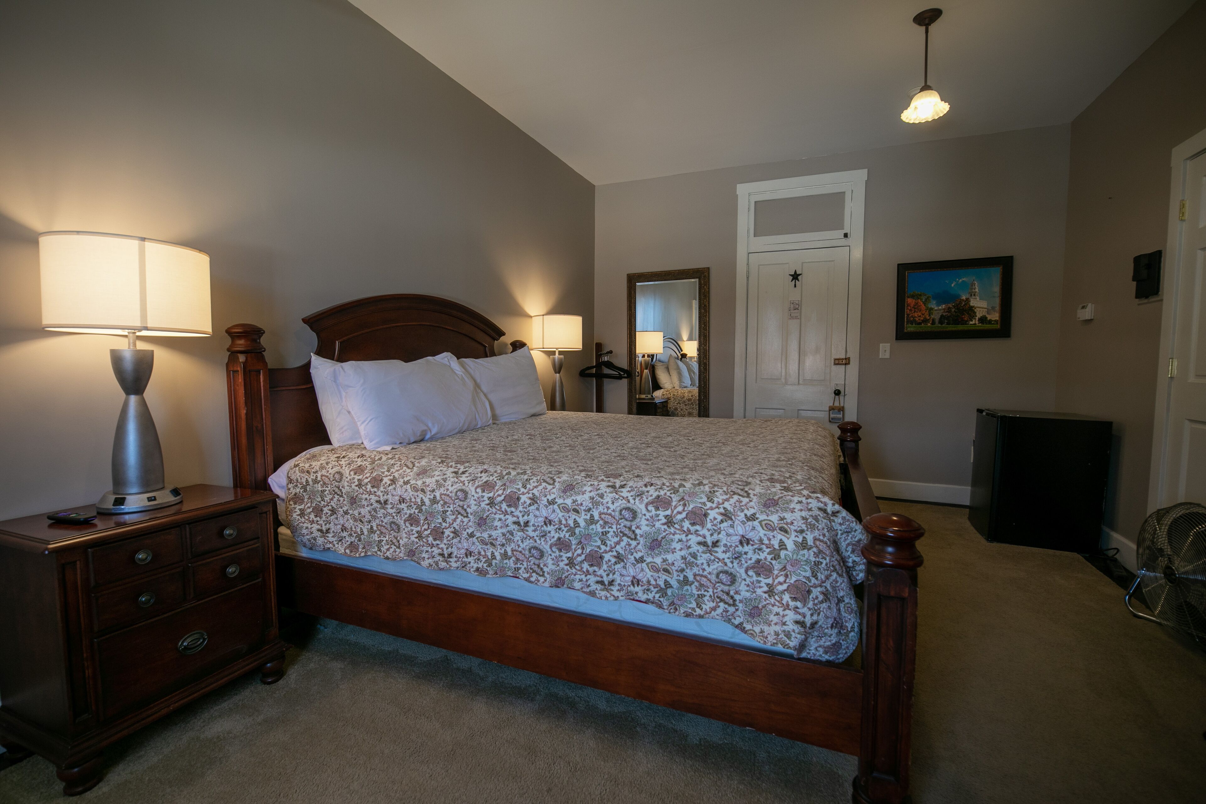 Un dormitorio con cama de madera, lámparas de noche, cómoda, espejo y una puerta.