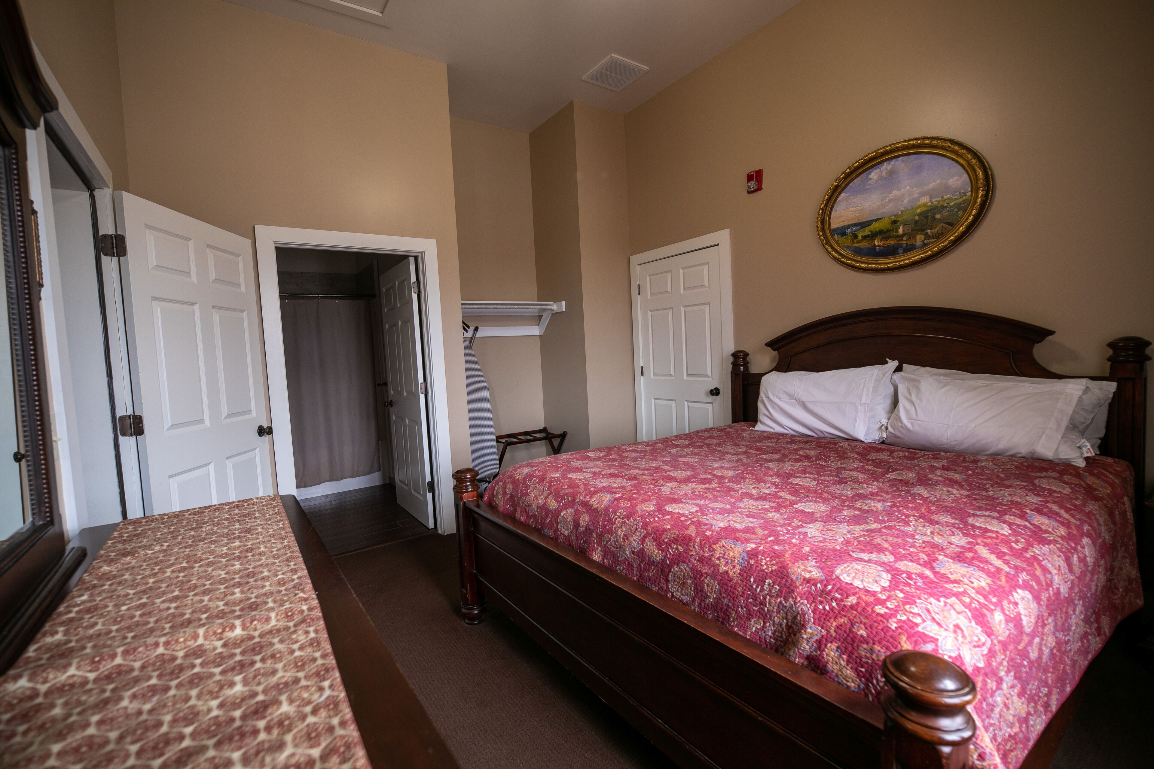 Quarto com cama de madeira, colcha estampada, um quadro na parede e porta que dá para outro cômodo.