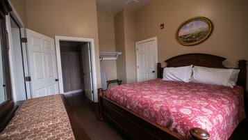 A bedroom with a wooden bed, a patterned bedspread, a painting on the wall, and a door leading to another room.