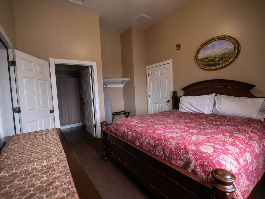 A bedroom with a wooden bed, a patterned bedspread, a painting on the wall, and a door leading to another room.