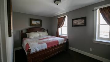 Quarto com cama de madeira, duas quadros na parede, janela com cortinas e luminária no teto.