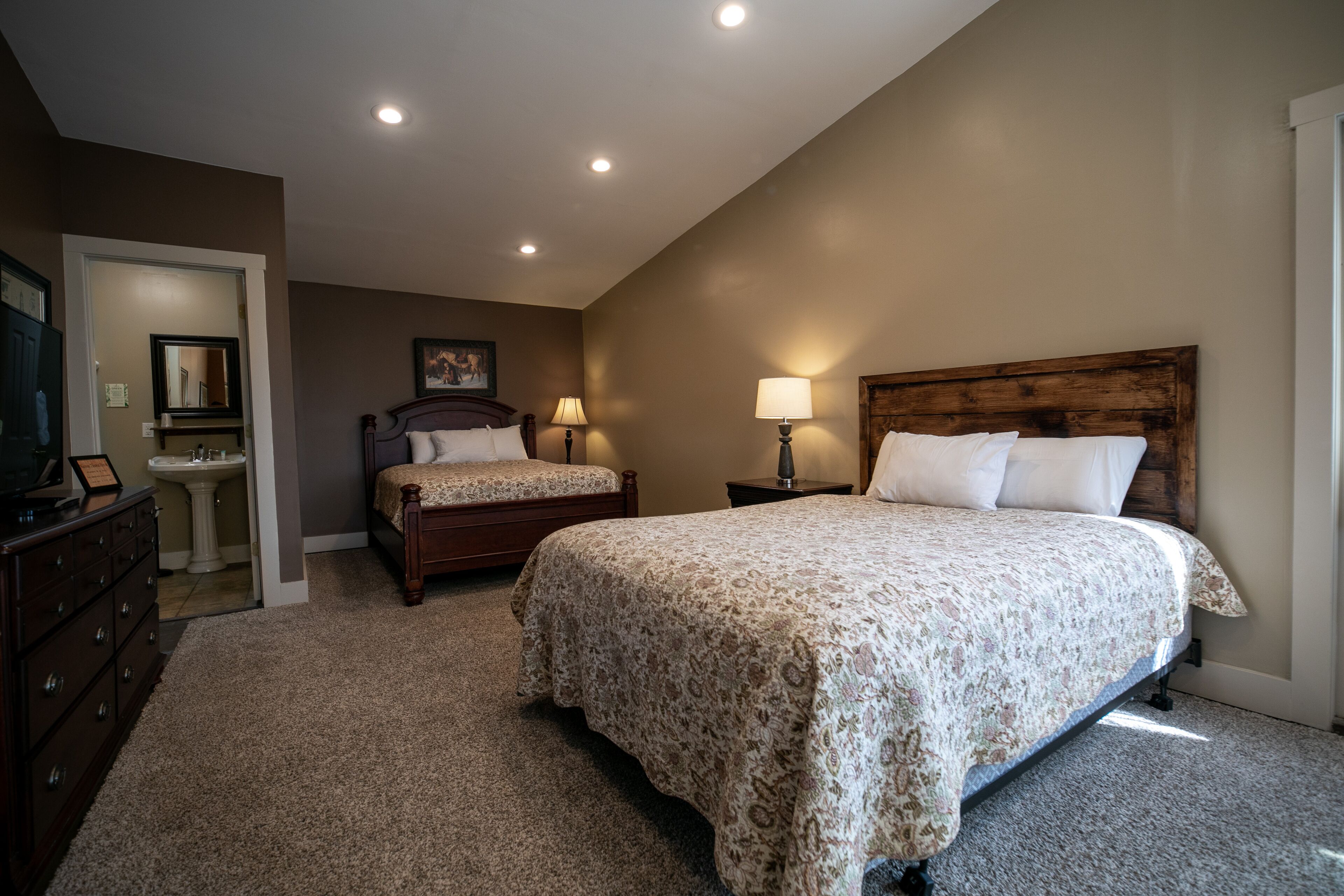 A bedroom with two beds, a dresser, a vanity, and a ceiling light.