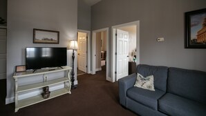 Un salon avec un téléviseur à écran plat posé sur une console blanche, un canapé gris et un tableau encadré accroché au mur.