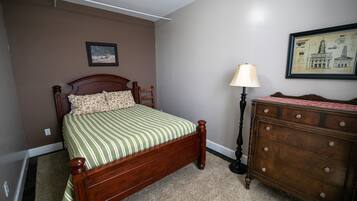 A bedroom with a wooden bed, a dresser, a lamp, and two framed pictures on the wall.