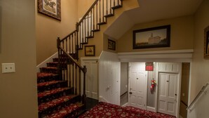 Un escalier dont les marches sont recouvertes d’une moquette rouge, menant à un palier avec des portes blanches et un panneau rouge indiquant la sortie.
