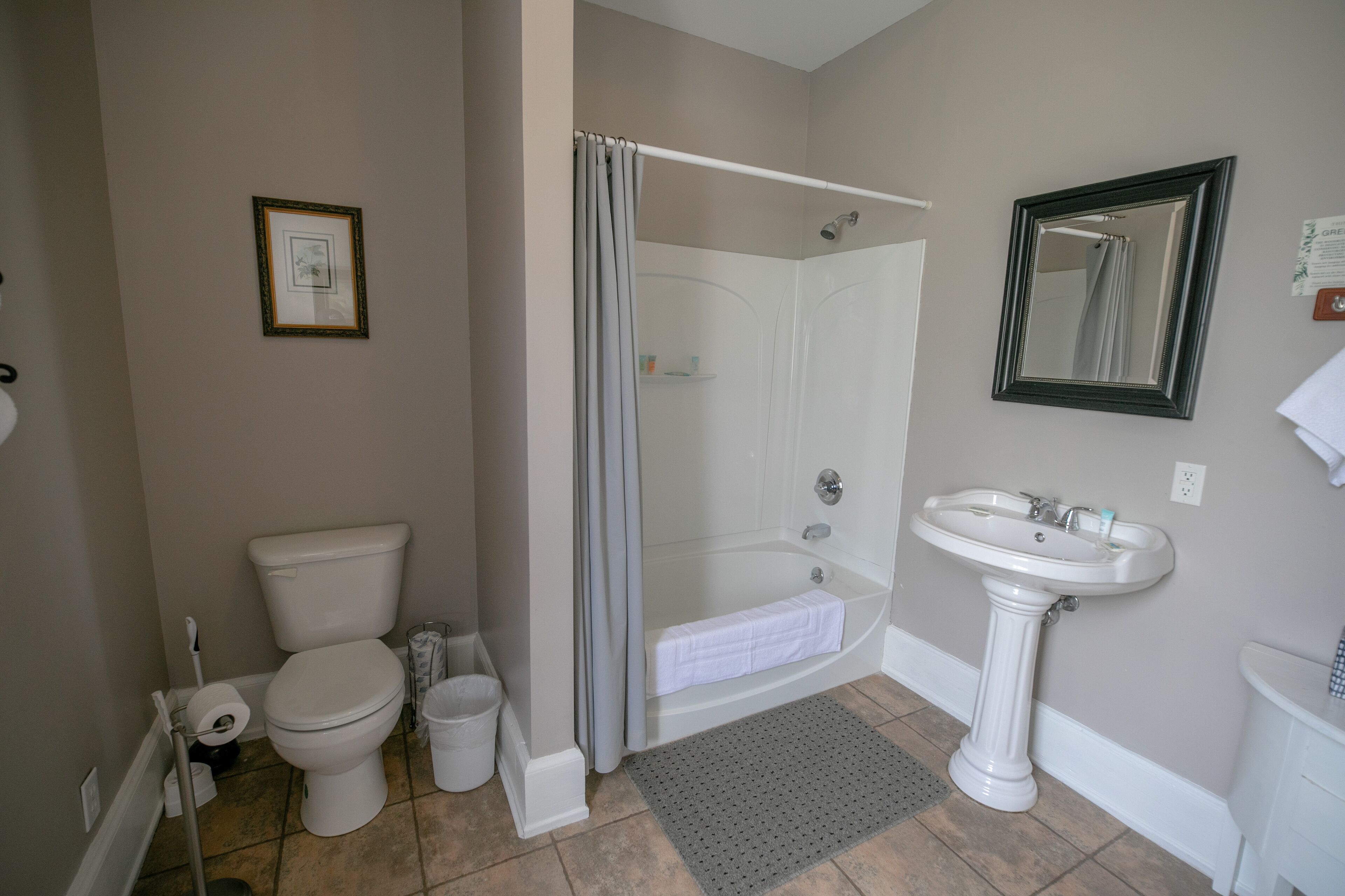 Une salle de bain équipée de toilettes, d’une douche, d’un lavabo et d’un tableau encadré au mur.