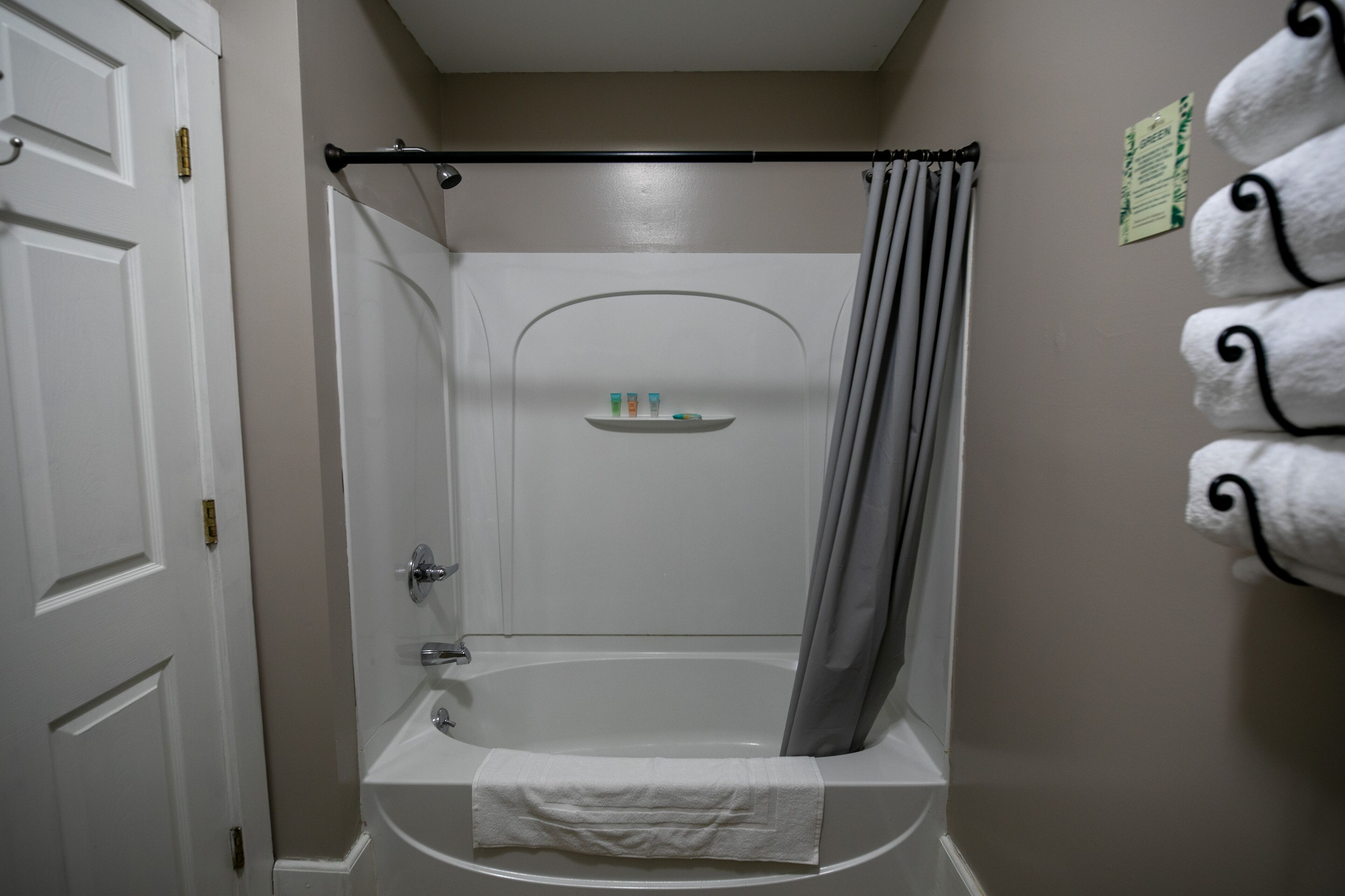 A bathroom with a bathtub, a shower curtain, a towel rack with towels, and a shelf with toiletries.