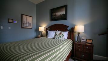 A neatly made bed with a striped bedspread, two bedside lamps, a framed picture above the bed, and a small dresser with a lamp on top.