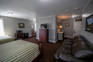 Habitación de hotel con dos camas, un sofá de cuero, un tocador, un televisor y un escritorio con lámpara.