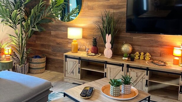 A modern living room with a wooden wall, a flat-screen TV, a round mirror, and a coffee table with a remote control. - Maison idéale pour les familles avec piscine privée - Fontaine-de-Vaucluse (Fontaine-de-Vaucluse)