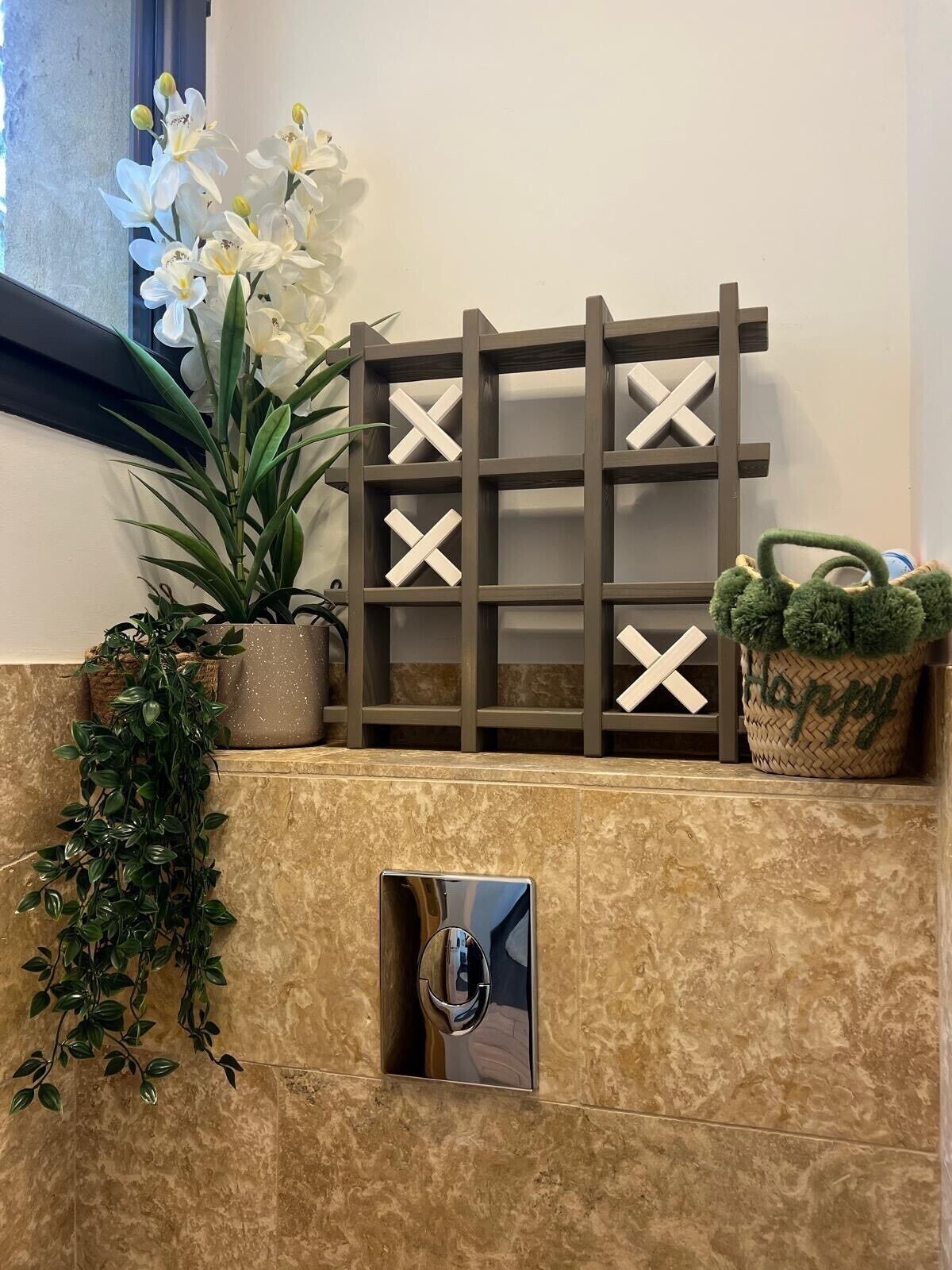 Un baño con pared de mármol, un espejo, una planta en maceta y un estante de madera decorativo.