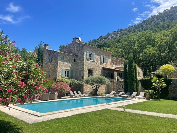 Una casa de piedra con piscina, rodeada de abundante vegetación y un paisaje montañoso.