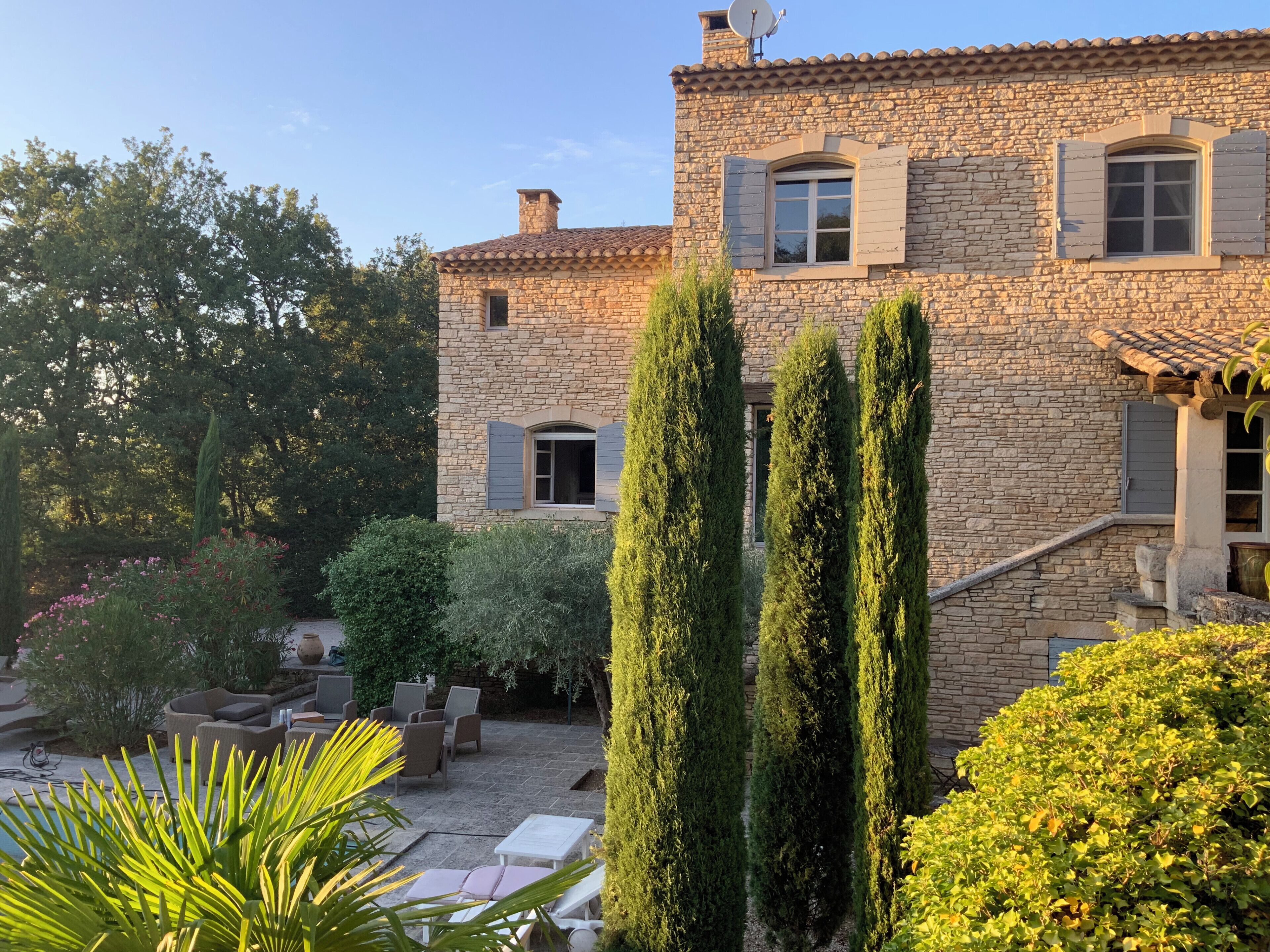 Un bâtiment en pierre doté d’une cour, d’un espace extérieur aménagé pour s’asseoir et de grands cyprès.