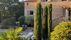 A stone building with a courtyard, outdoor seating, and tall cypress trees. - Propriété d'exception au coeur du Luberon (Robion)