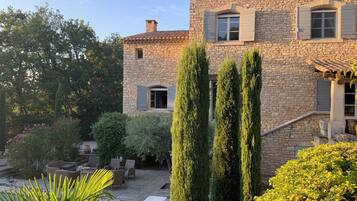 Un bâtiment en pierre doté d’une cour, d’un espace extérieur aménagé pour s’asseoir et de grands cyprès.
