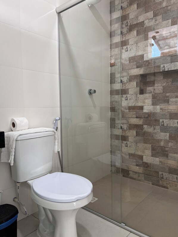 Un baño con inodoro, cabina de ducha de vidrio y pared de azulejos con diseño de ladrillo.
