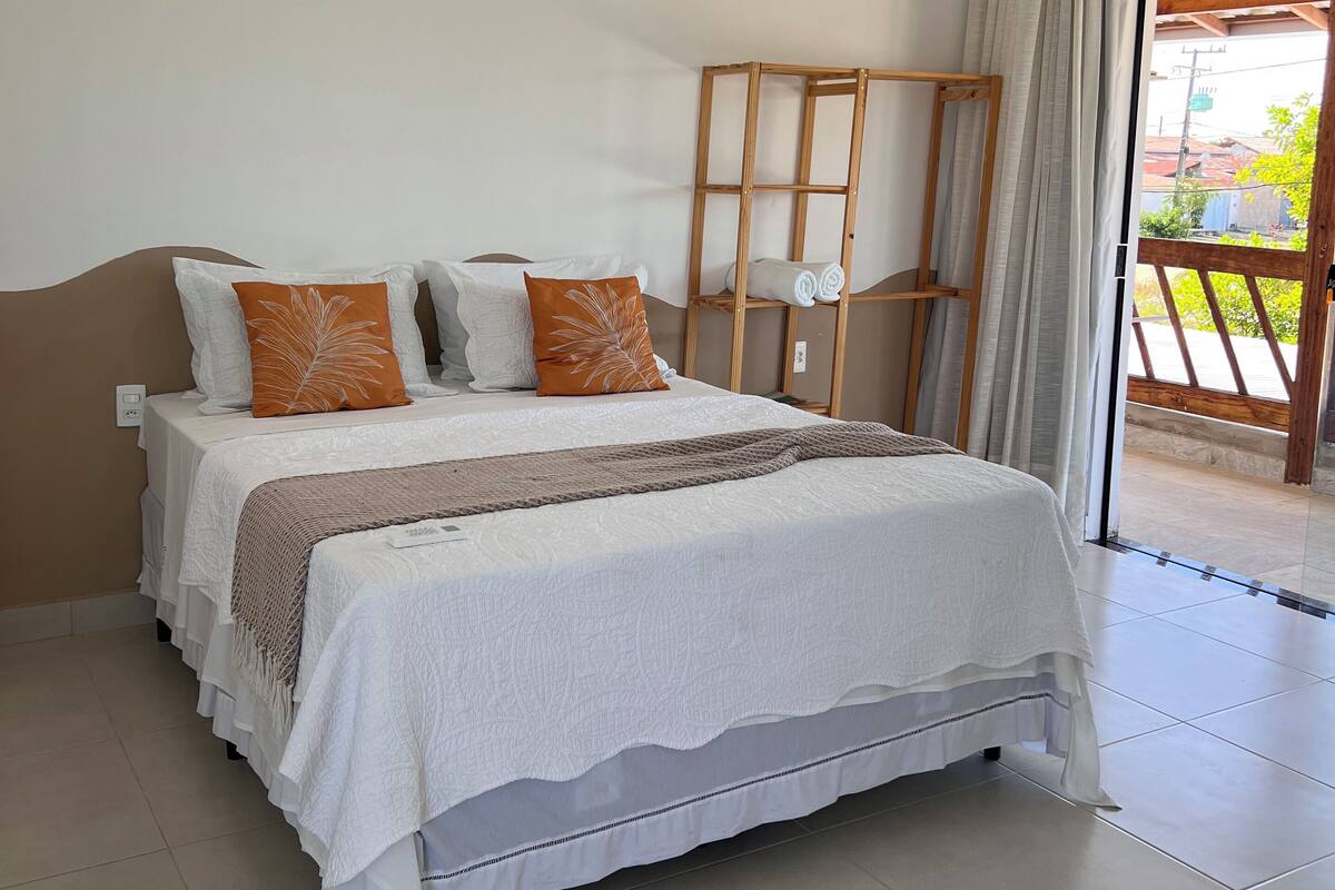 A bedroom with a bed, pillows, a wooden ladder, and a view of the outside.