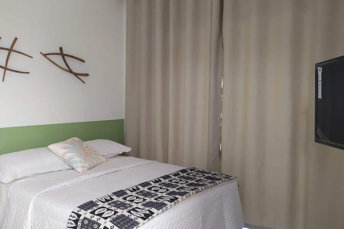 A hotel room with a bed, a green wall, and a curtain.