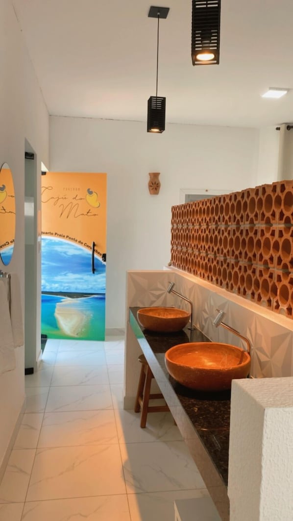 A bathroom with two large, round, terracotta sinks, a wooden decorative wall, and a mural of a beach scene on the wall. - Pousada Caju do Mato (Prado)