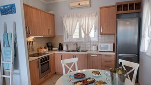 A modern kitchen with wooden cabinets, a stainless steel refrigerator, and a dining table set with food and drinks. - Villa Pasithea - breathtaking seaviews, infinity pool, privacy, close to beach (Perigiali)
