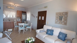 A living room with a white sofa, a coffee table with flowers, and a dining area with a table and chairs. - Villa Pasithea - breathtaking seaviews, infinity pool, privacy, close to beach (Perigiali)