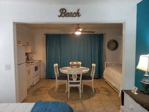 A compact room with a kitchenette, a dining area with a table and chairs, a bed, and a ceiling fan.