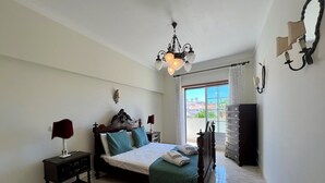 A bedroom with a bed, bedside tables, a chandelier, a dresser, and a view of the outside. - LAGOS TYPICAL HOUSE by HOMING (Lagos)
