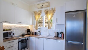 Een moderne keuken met witte kastjes, een roestvrijstalen koelkast, een ingebouwde oven, een magnetron, en een spatwand van natuursteen.