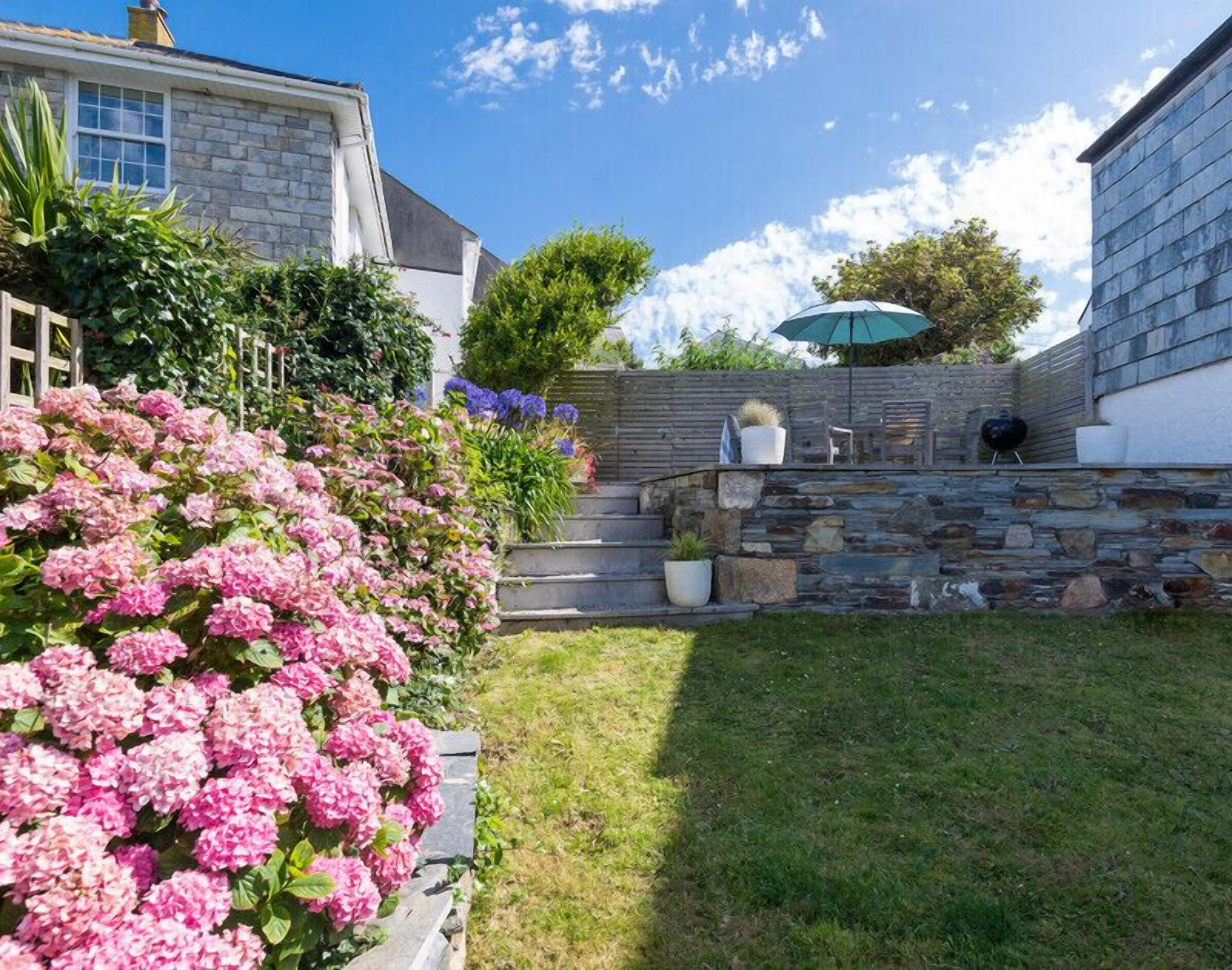 A stone wall with a barbecue grill, outdoor seating, and a garden with pink flowers.