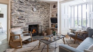 A cozy living room with a stone wall, a fireplace, a television, and comfortable seating. - Albany (Port Isaac)