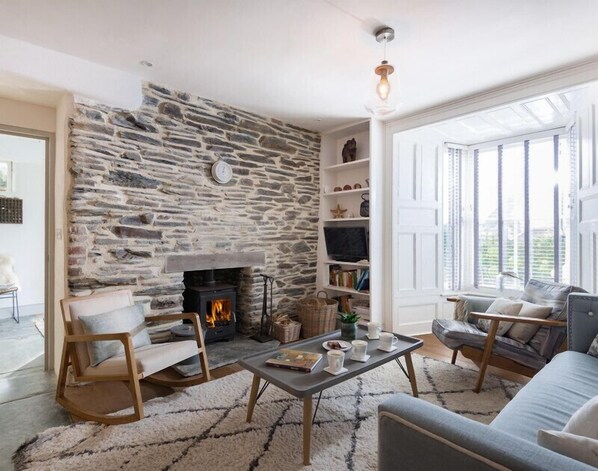 A cozy living room with a stone wall, a fireplace, a television, and comfortable seating. - Albany (Port Isaac)