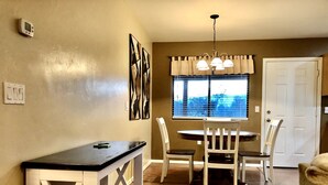 Un espace repas comprenant une table et des chaises, une fenêtre avec des stores, une porte et un luminaire fixé au mur.