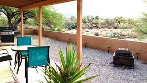 Une terrasse extérieure équipée d’un barbecue, de chaises et offrant une vue sur la végétation désertique.