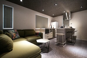A compact living space with a sofa, a small table, a kitchenette, and two bar stools. - Real Life Aoyama 2BR Suite 5pax 3bed 3min Metro (Tokyo)