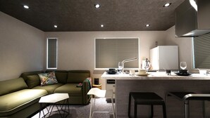 Una cucina moderna con frigorifero integrato, zona pranzo con tavolo bianco e sgabelli da bar, divano verde con cuscini decorati e una finestra con tende.