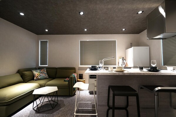 A modern kitchen with a built-in refrigerator, a dining area with a white table and bar stools, a green sofa with patterned cushions, and a window with blinds. - Real Life Aoyama 2BR Suite 5pax 3bed 3min Metro (Tokyo)