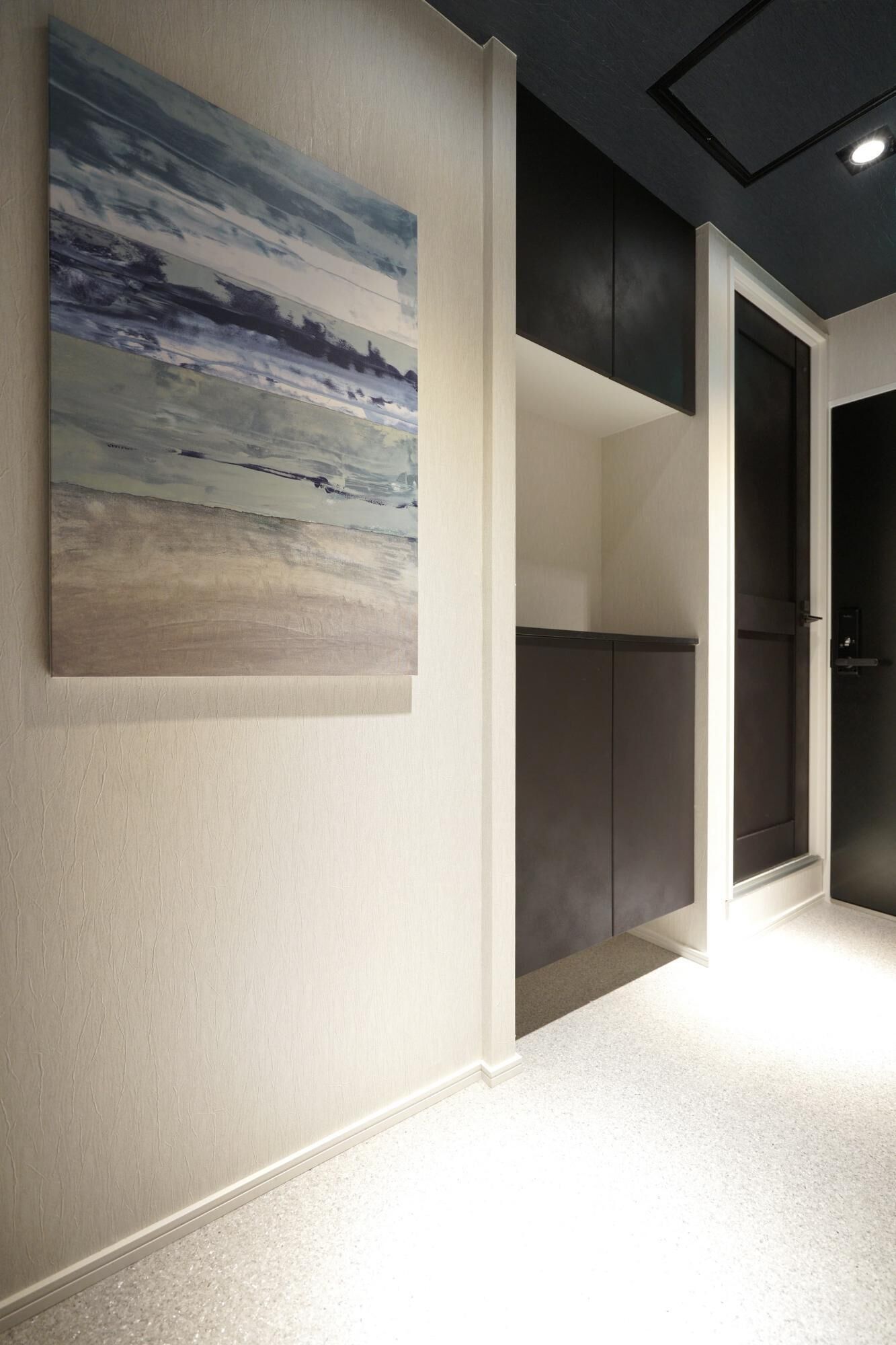 A hallway with a large abstract painting on the wall, a dark door, and a light-colored carpet.