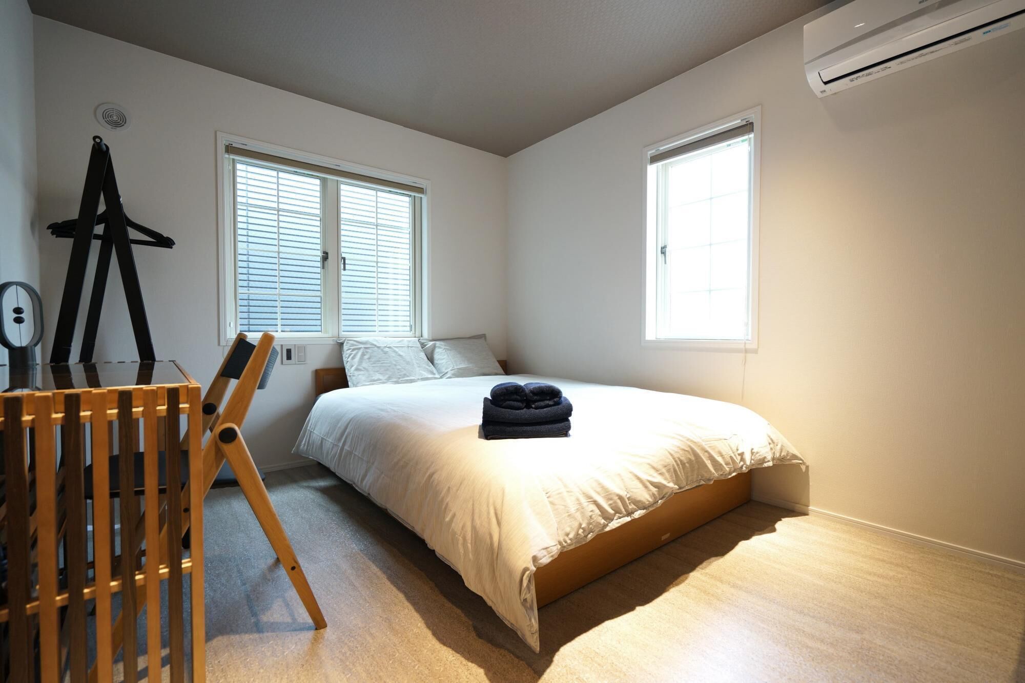 Une chambre à coucher avec un lit, deux fenêtres, un climatiseur et une chaise en bois.