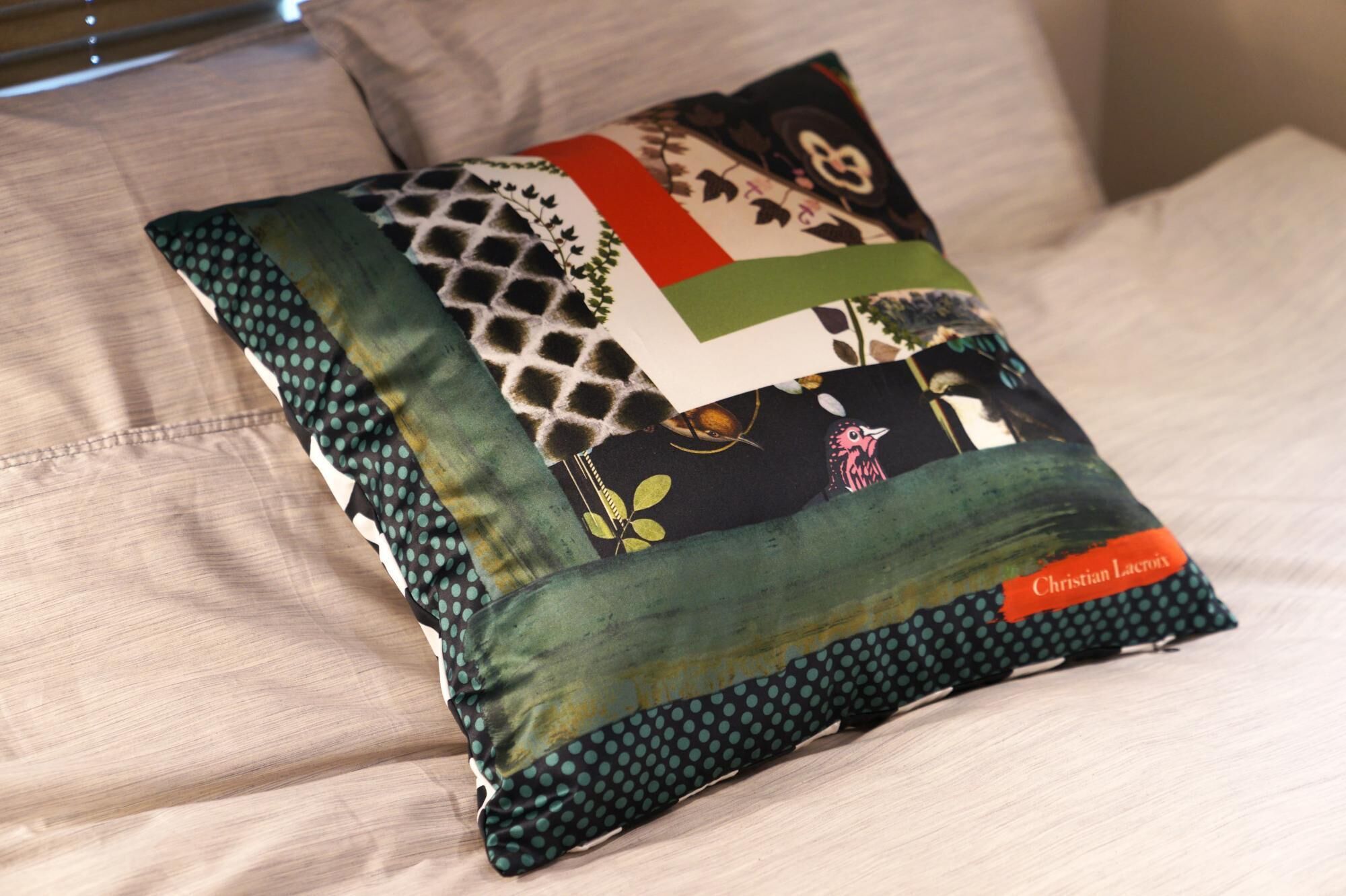 A patchwork pillow with various patterns and a label reading "Christian Lacroix" on a light-colored sofa.