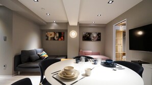 Un salon moderne avec une table de salle à manger ronde, des chaises noires, un canapé et un téléviseur fixé au mur.