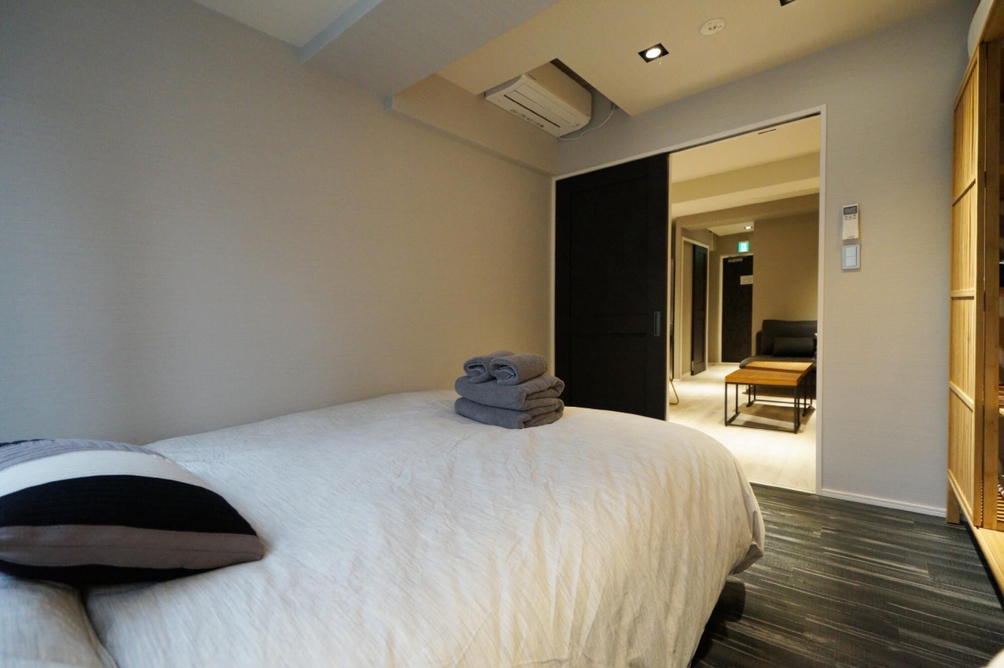 Una habitación de hotel con una cama bien hecha, una mesita pequeña y un suelo de madera oscura.