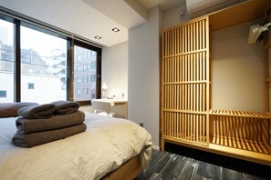 A modern hotel room with a large bed, a wooden wardrobe, a desk with a lamp, and a view of buildings through large windows. - Real Life Kudanshita Chic 2-bedroom 6pax 3mins sub (Tokyo)