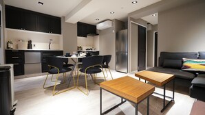 Une cuisine moderne avec des meubles de couleur sombre, un coin repas avec des chaises, un réfrigérateur et un canapé dans l’espace salon.