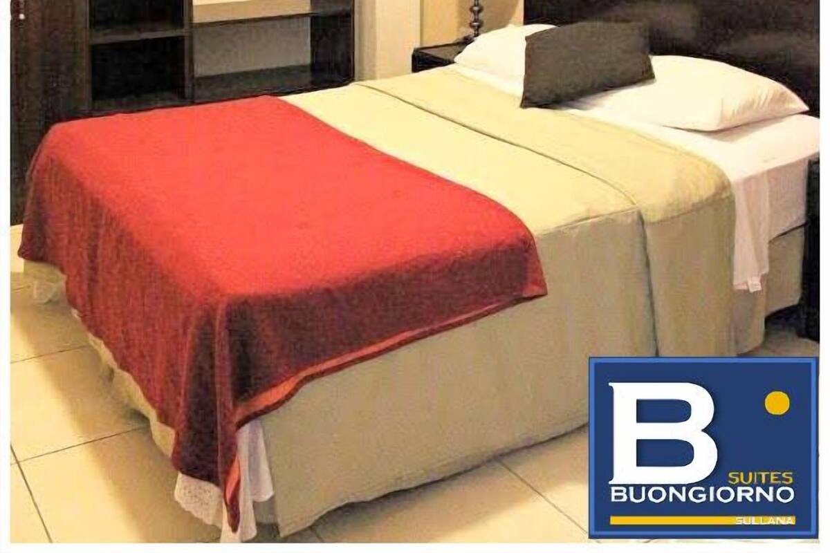 Ein Schlafzimmer mit einem Bett, einem Nachttisch mit Lampe, einem Kleiderschrank, einem Deckenventilator und einem gerahmten Bild an der Wand.