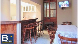 A dining area with wooden chairs and a table, a kitchen with cabinets, and a television mounted on the wall. - Buongiorno Suites Sullana I (Sullana)