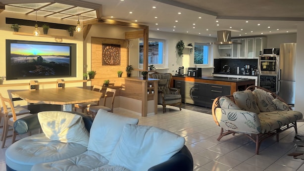 A modern living room with a dining area, kitchen, and a large flat-screen TV mounted on the wall.