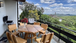 A wooden table and chairs on a balcony with a view of a green landscape and mountains.