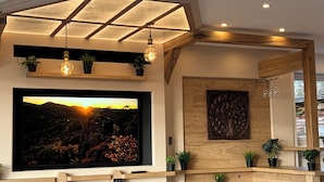 A modern dining area with a large TV, wooden furniture, and potted plants.