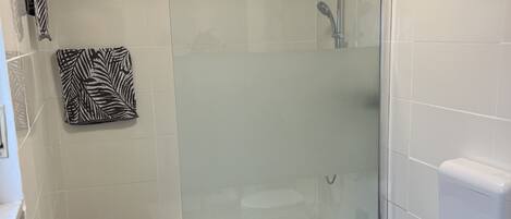 Un baño moderno con cabina de ducha de vidrio, inodoro blanco y felpudo negro.